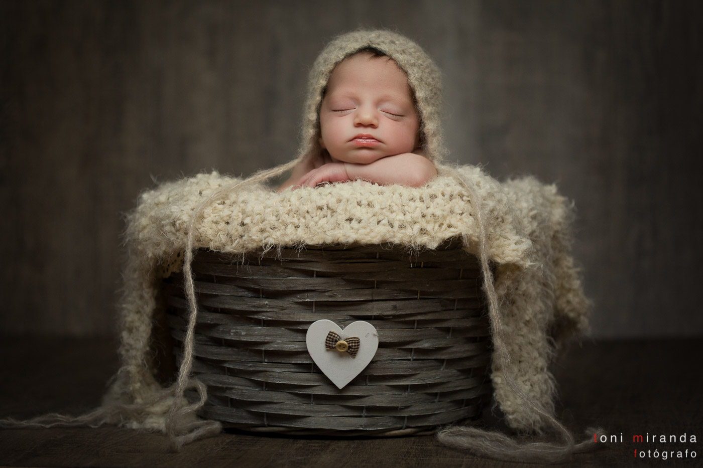 recién nacida en cesta durmiendo con gorro de lana fondo gris
